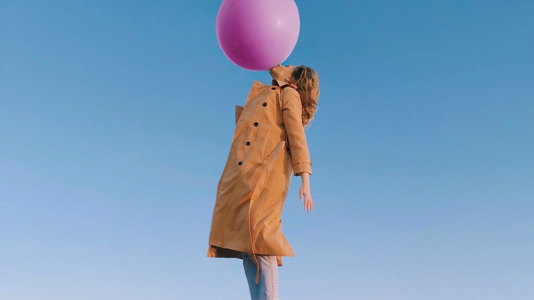 young female blowing huge balloon in sky