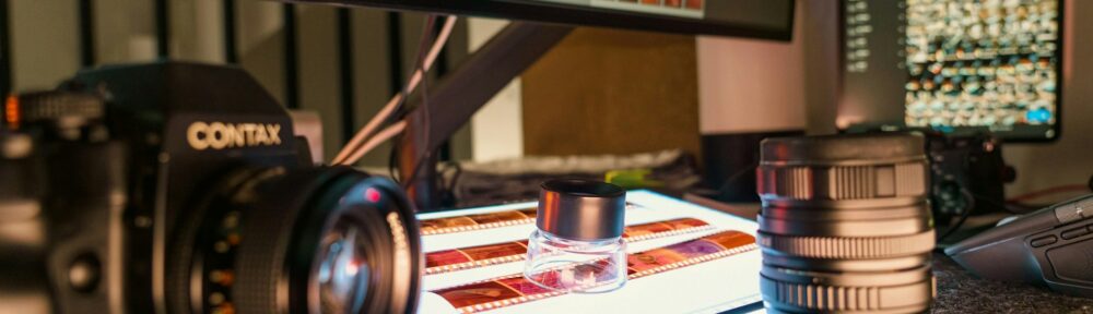 Tavolo di lavoro con negativi sotto la lente e provini in fila sul monitor, lo sguardo che manca alle classifiche dei migliori registi