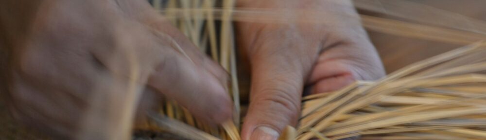 Due mani che intrecciano fili di paglia su una stuoia, l'immagine di Gandhi e il lavoro che passa dalle mani
