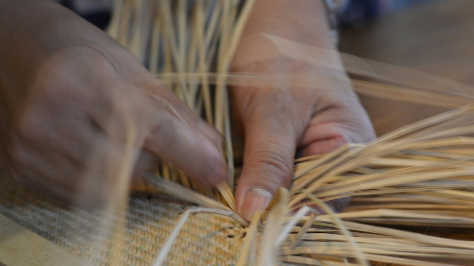 Due mani che intrecciano fili di paglia su una stuoia, l’immagine di Gandhi e il lavoro che passa dalle mani