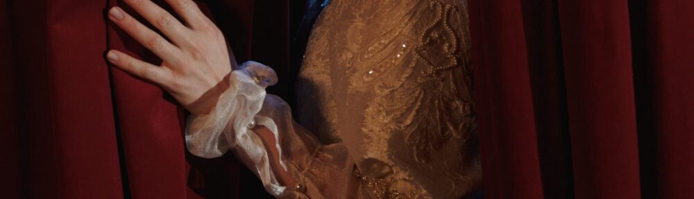 Mano di attrice che scosta il sipario rosso un attimo prima di entrare in scena, immagine per i corti teatrali
