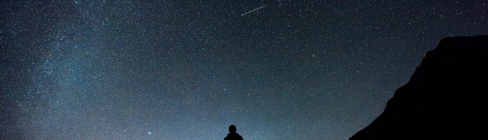Un uomo solo in piedi su una collina guarda il cielo stellato, il canto di Dio nello spazio aperto sopra di lui