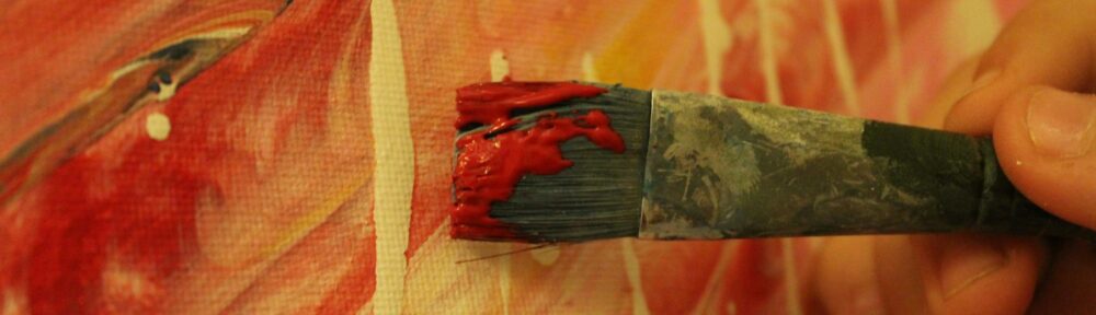 Un pennello carico di colore rosso appoggiato su una tela dipinta, immagine dell'attore come mezzo artista