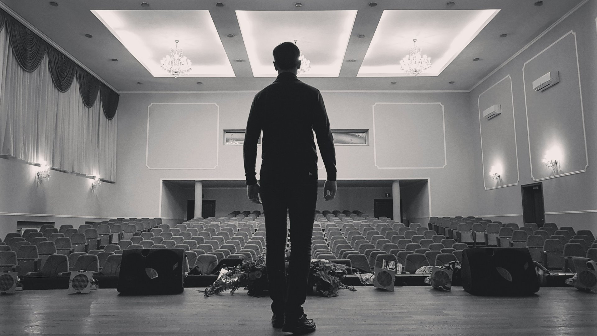 Un uomo solo in piedi sul palco di una produzione artistica guarda le poltrone vuote della platea