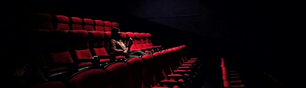 Una spettatrice sola in una sala cinematografica vuota, tra le poltrone rosse al buio