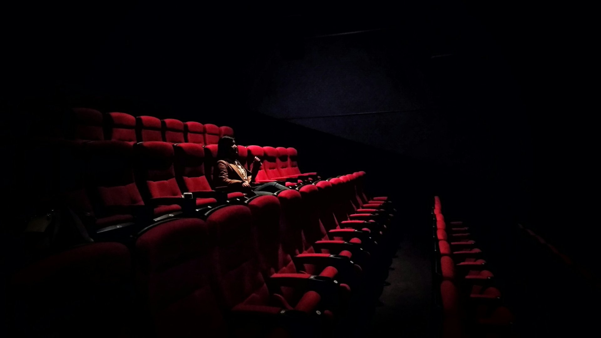 Una spettatrice sola in una sala cinematografica vuota, tra le poltrone rosse al buio