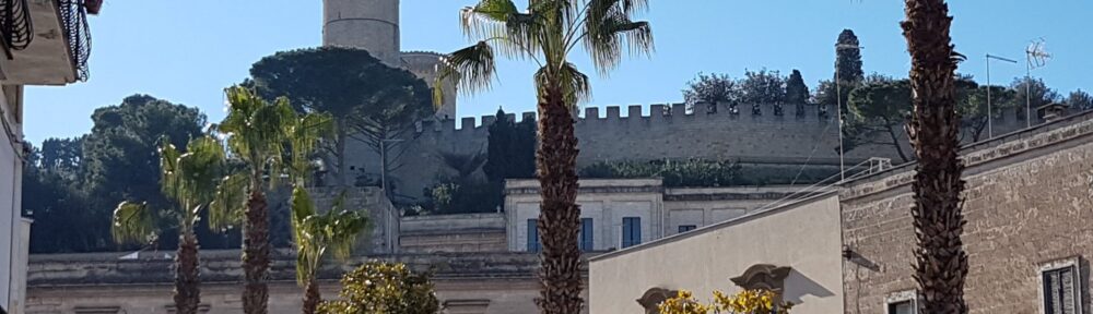 Il castello di Oria visto dalle palme di piazza Lama, i luoghi dei libri per conoscere Oria