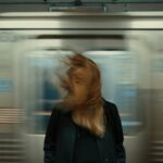 Una donna ferma sulla banchina della metro mentre un treno le sfreccia alle spalle e le scompiglia i capelli: immagine dell'articolo su Stanislav Petrov e sul fermarsi a pensare