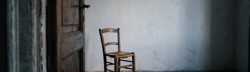 Una porta socchiusa su una stanza spoglia, con una sedia impagliata vuota davanti al muro: immagine della pratica dell'attore
