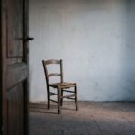 Una porta socchiusa su una stanza spoglia, con una sedia impagliata vuota davanti al muro: immagine della pratica dell'attore