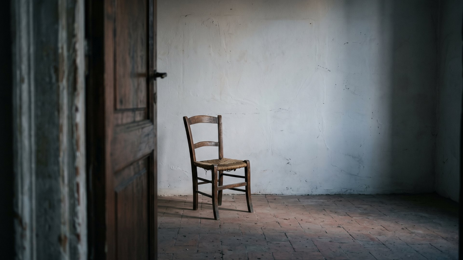 Una porta socchiusa su una stanza spoglia, con una sedia impagliata vuota davanti al muro: immagine della pratica dell'attore